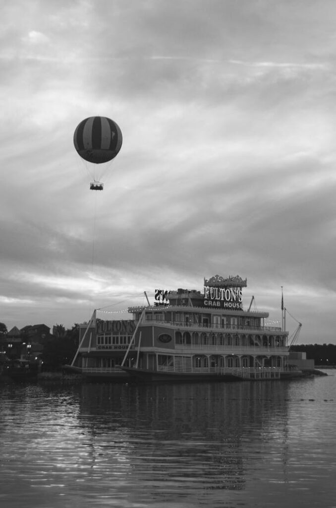 A striking black and white photo of a hot air balloon floating above Fulton's Crab House on a river.